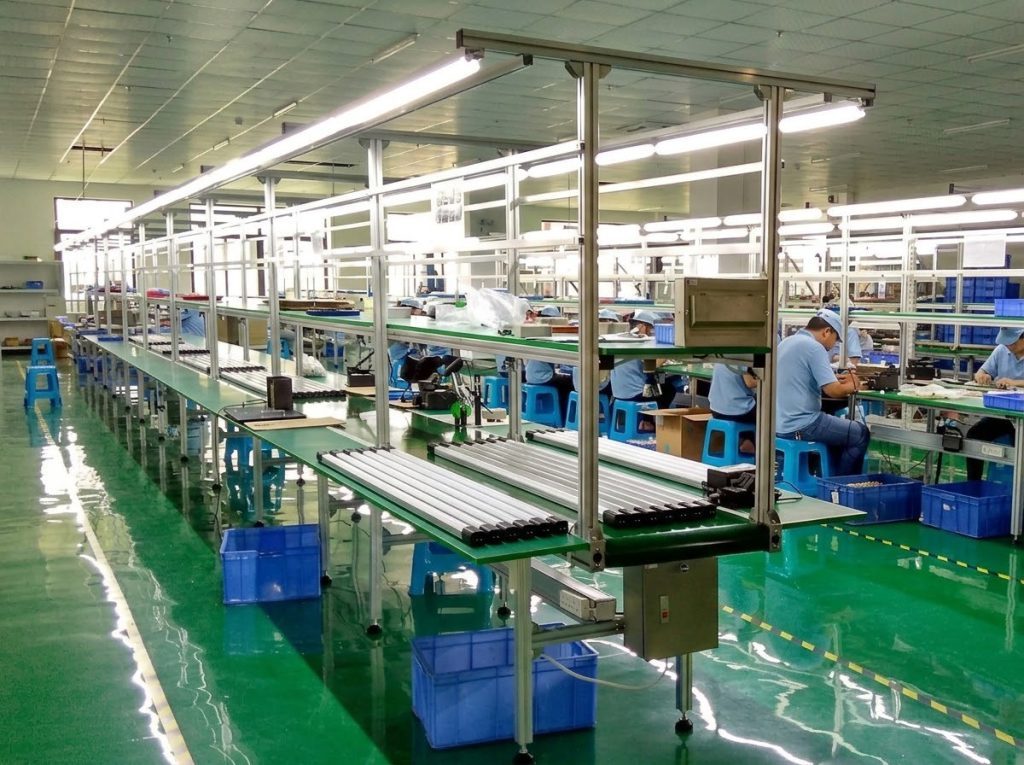 Inside view of our lighting factory assembly line in Zhongshan, with workers installing chandelier components on a multi-station production line.